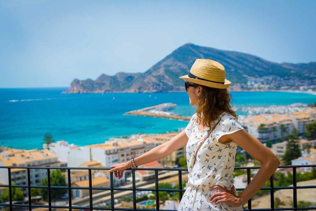 Tourist woman with straw sunhat looking to the mediterranean sea and enjoying the blue and scenic seascape in Altea, Alicante, Spain