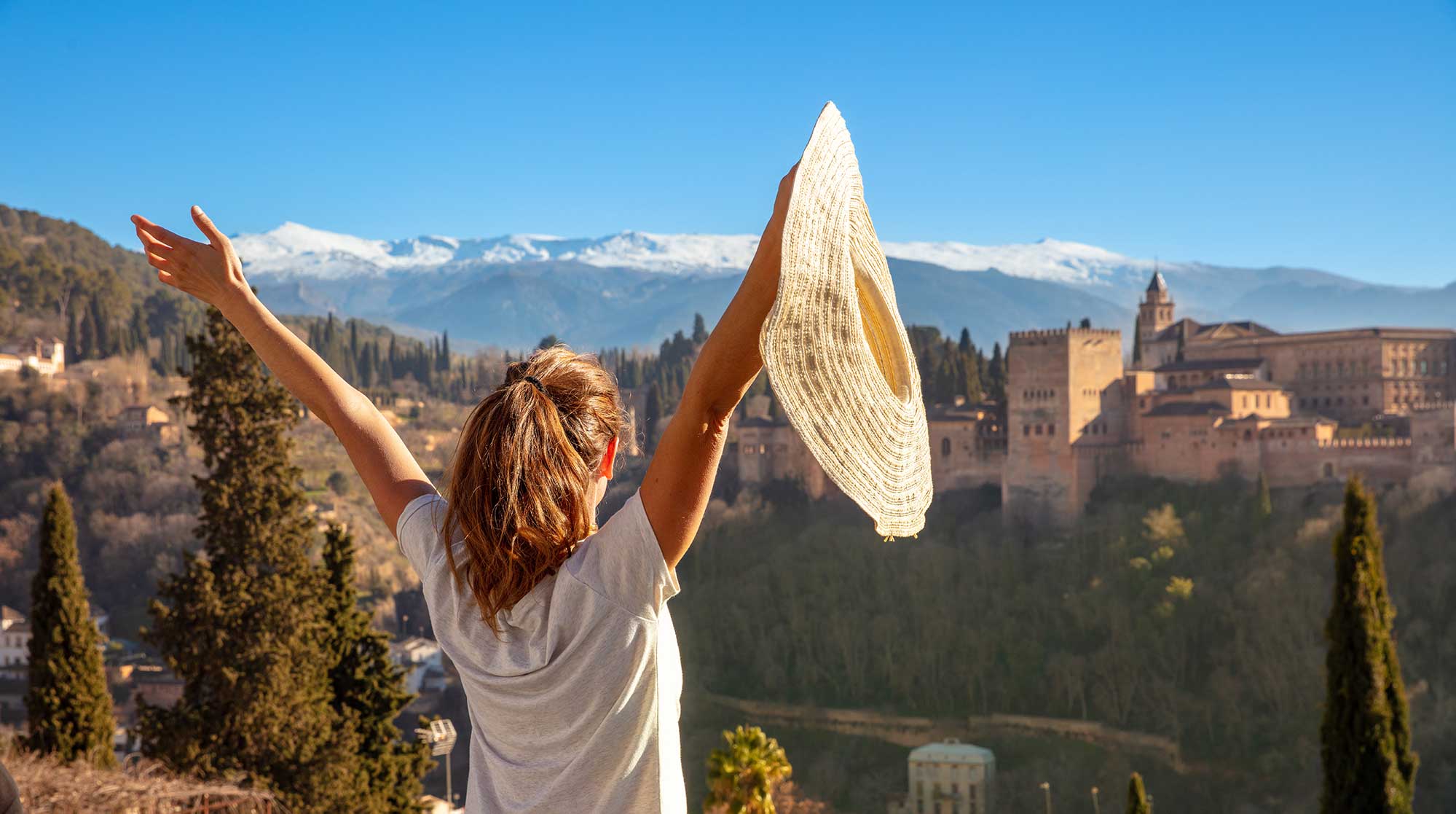 guest on tour gazing at the alhambra palace with mountain range in background.