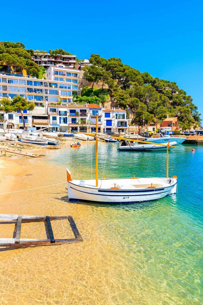 Fishing boat on beach in Llarfanc town with colorful houses in background, Costa Brava, Spain_